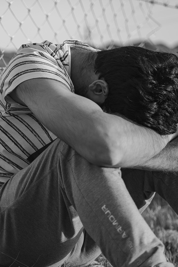 A man wearing stripe shirt in a black and white color sitting on the ground with his head in his hands.