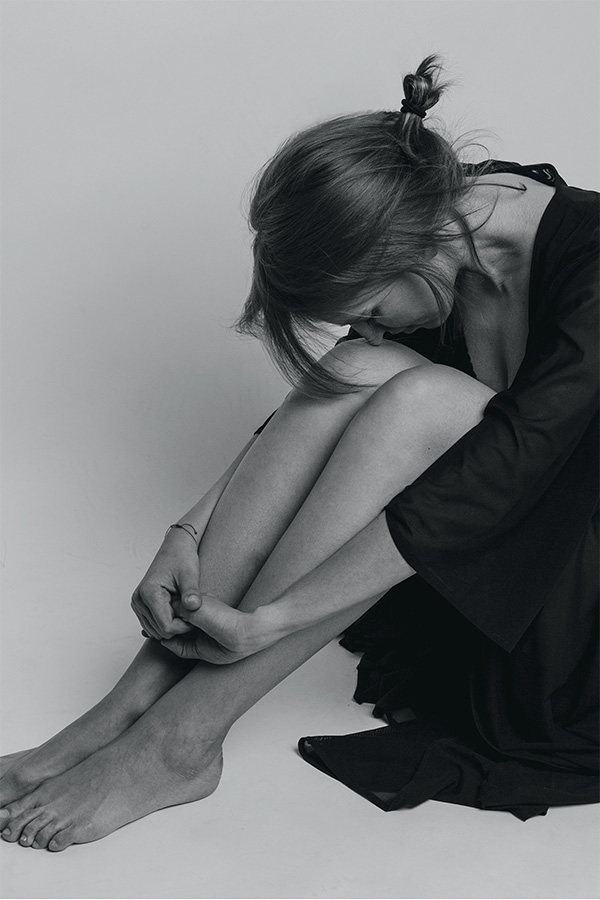 A girl sits on the floor with knees pulled into her chest and head drooped before trying accelerated TMS therapy. 