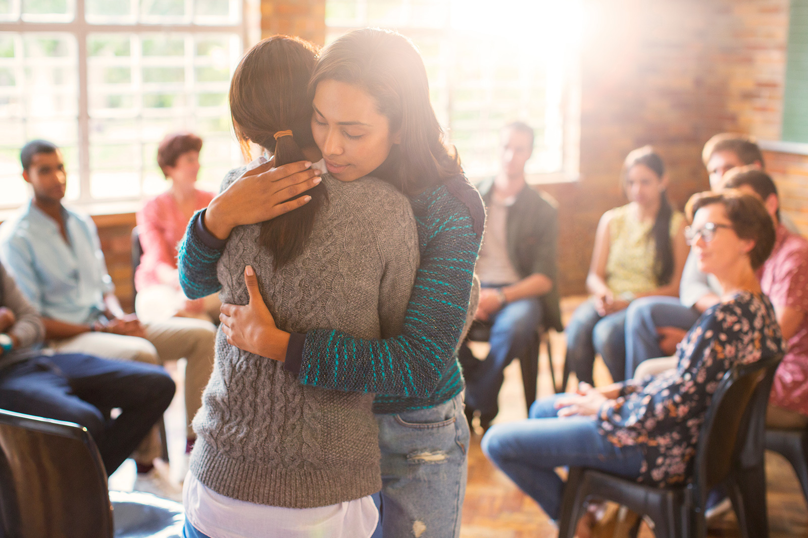 Two females hug in a group therapy session; one of many types of treatments for depression. 