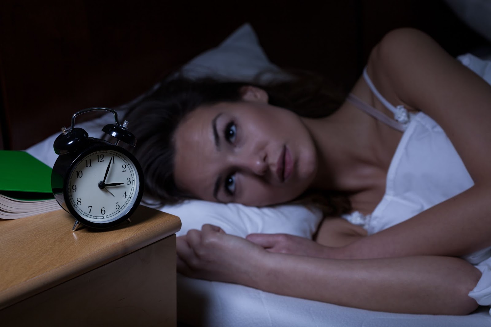 A woman lying in bed, staring at an alarm clock, representing insomnia and possibly undergoing TMS therapy for ADHD