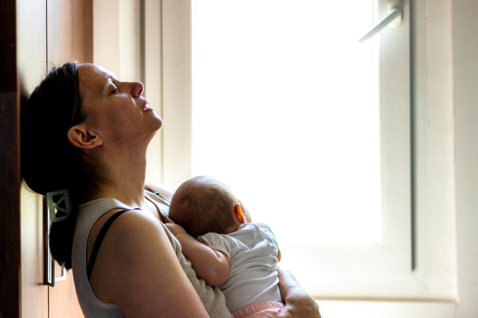Mother cradling baby at window shows bond and postpartum challenges
