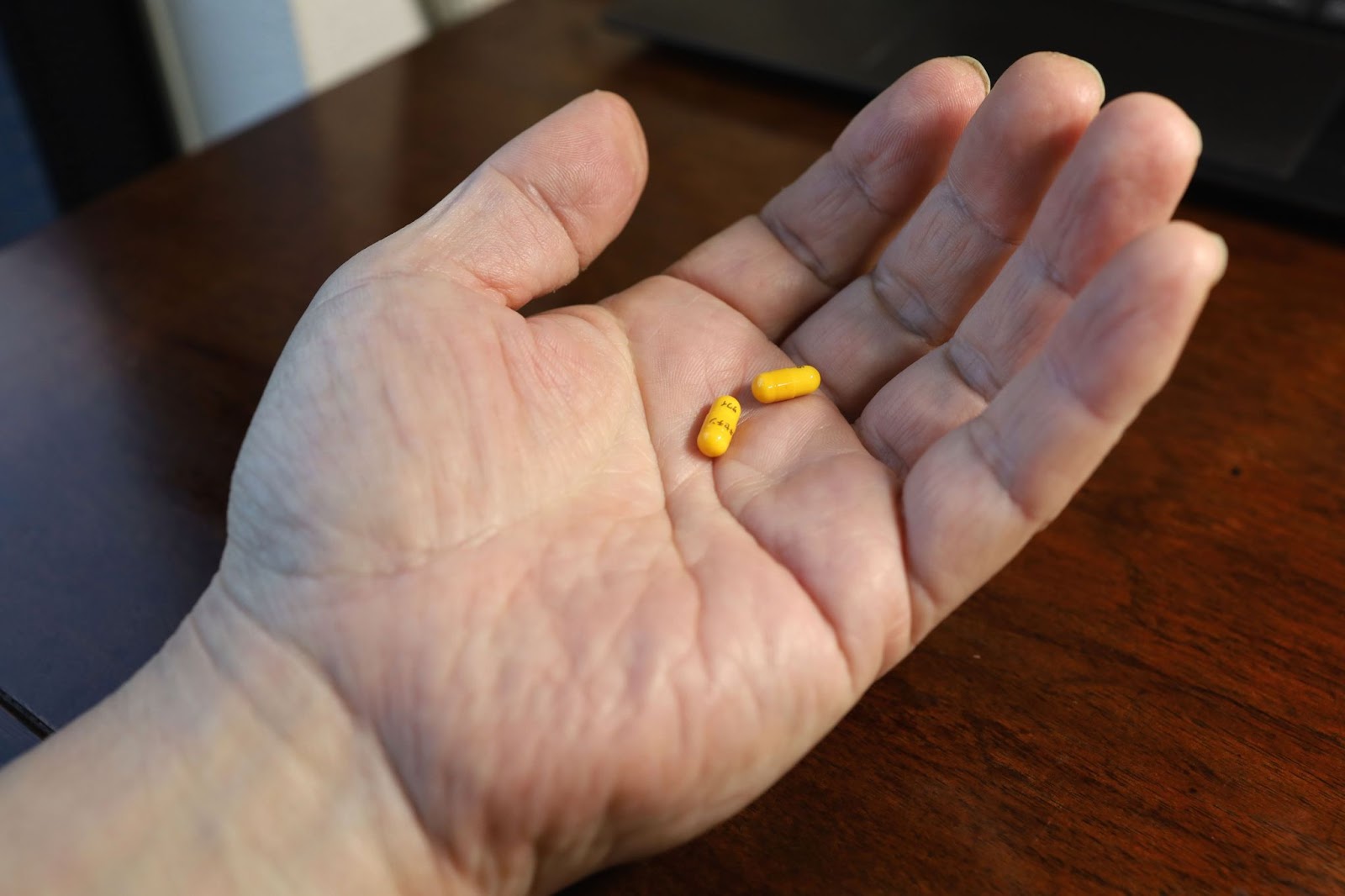 A hand holds a yellow pill in front of a laptop, with TMS therapy, ADHD, ADHD medication in mind.