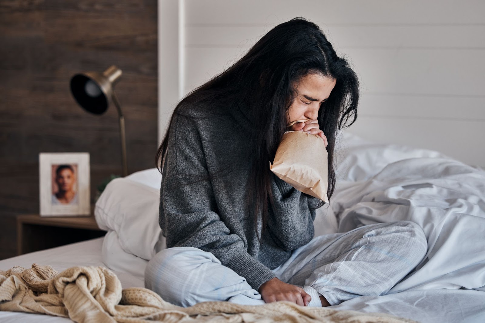 A woman sitting on a bed with a pillow, receiving TMS therapy for panic disorder and panic attacks.