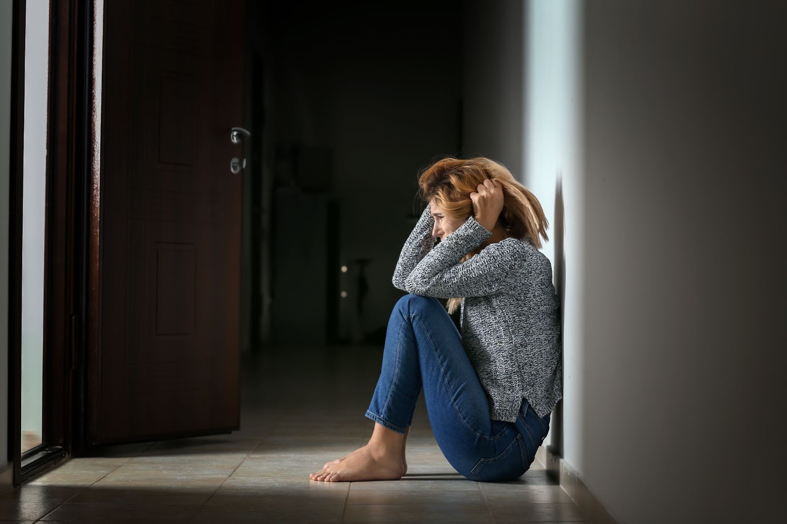 A woman with panic disorder sits on the floor in an empty room, seeking relief through TMS therapy.