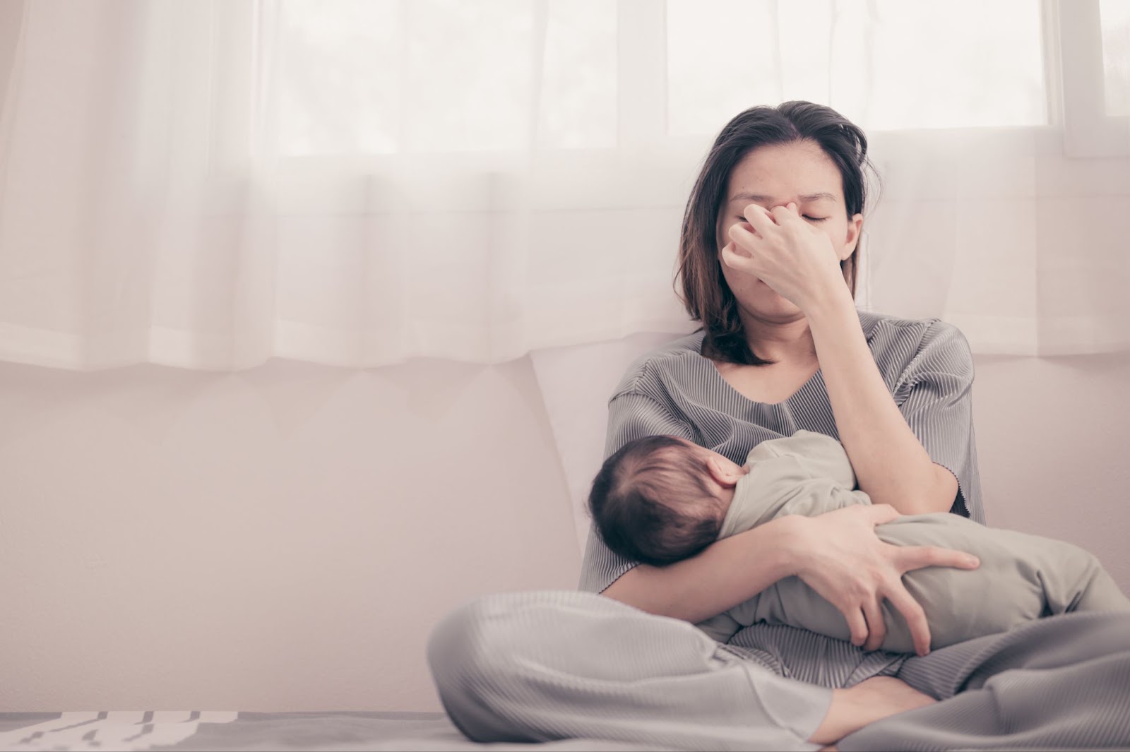 A woman sitting on a bed holding her baby, receiving TMS therapy for postpartum depression.