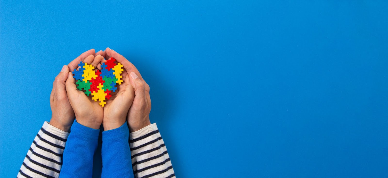 Children's hands holding colorful puzzle pieces on blue background.