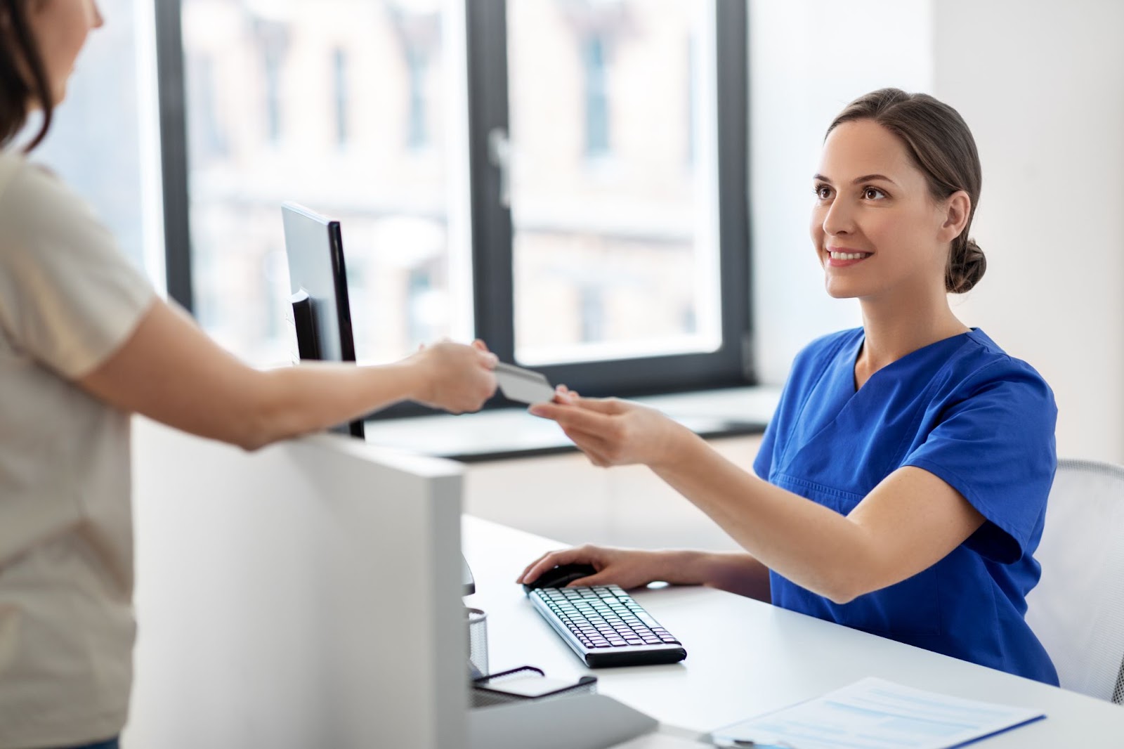 Two women in scrubs exchange a credit card. TMS therapy, postpartum depression, postpartum.