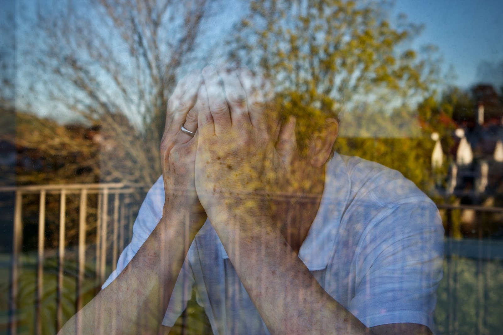 A man gazes out the window, hands on his face, reflecting on his thoughts related to TMS therapy and suicide ideation.