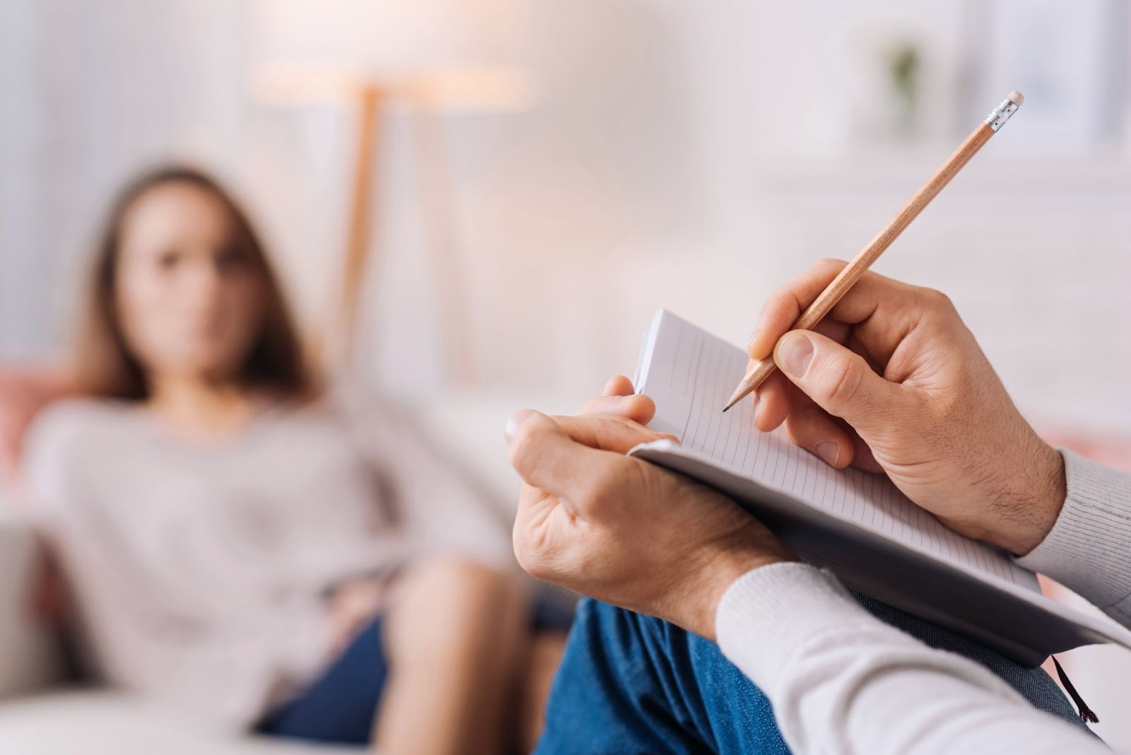 A man writes in a notebook while his girlfriend relaxes on the couch, symbolizing support during TMS therapy for anxiety and depression.