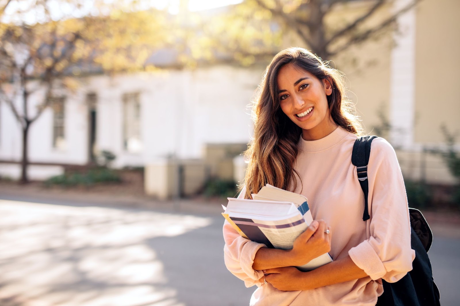 A smiling young woman holds books, radiating positivity, symbolizing hope in overcoming anxiety and depression through TMS therapy.