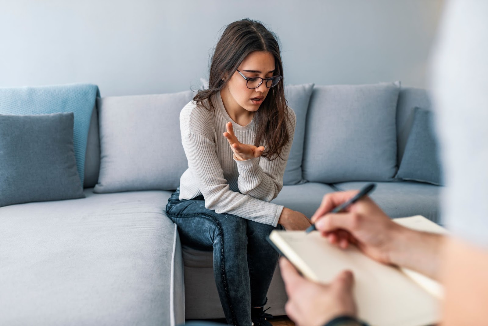 A woman converses with a man on a couch, highlighting the supportive environment of TMS therapy for anxiety and depression.