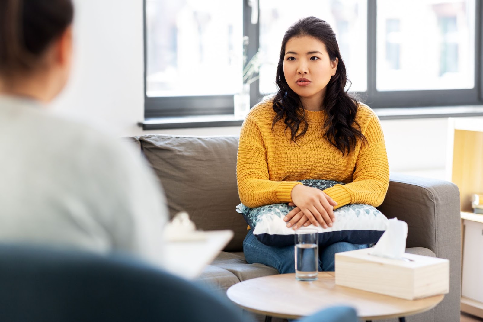 A woman sits on a couch, holding a cup of coffee, reflecting on her journey with TMS therapy for anxiety and depression.