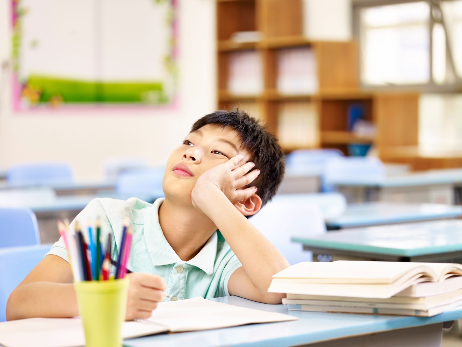 A boy rests his head on his hand at a desk, reflecting the challenges of ADHD and the potential of TMS therapy.