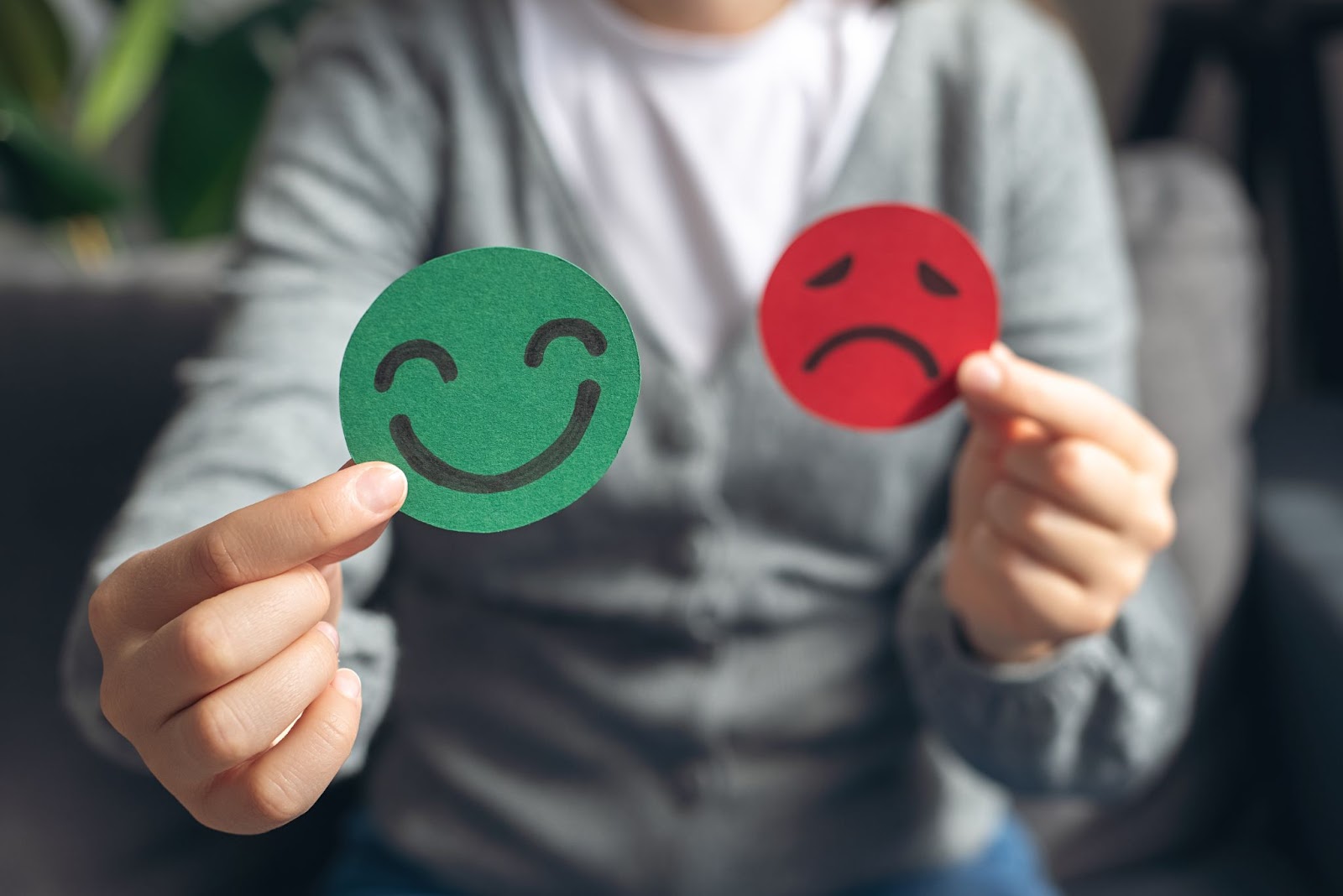 A woman holds two smiley faces, one red and one green, symbolizing emotions related to bipolar disorder and TMS therapy.