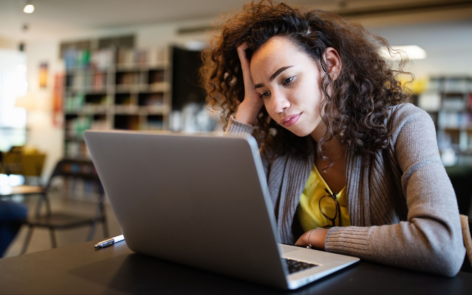 A woman with ADHD rests her head on her hand while focused on her laptop at a table, reflecting on TMS therapy.