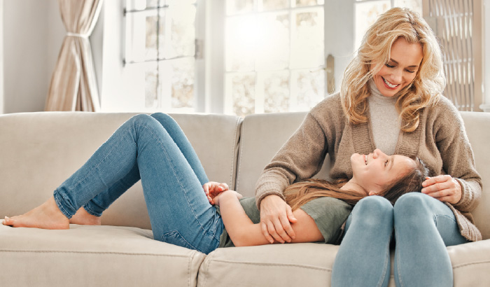 A child on a couch rests her head on her mother’s lap.